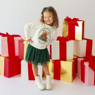 Model wearing Sweet Wink sequin Christmas tree patch sweatshirt with emerald rhinestones, festive holiday design, and a white bow headband.