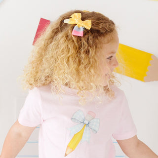 Sweet Wink School Days Pencil Bow Clip Set
Child wearing a pink shirt with colorful pencil design, sitting on a white surface.