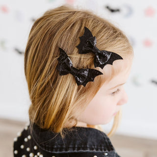 Sweet Wink Glitter Bat Halloween Bow Clip Set
A young girl with blonde hair shown from the side, wearing two black bat-shaped hair clips with a glittery finish.