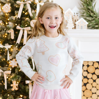 Model wearing a blush pink Christmas cookies sweater by Sweet Wink, paired with a tutu skirt and festive bows.