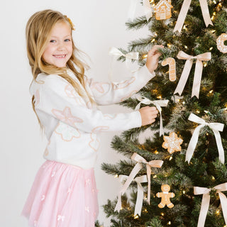 Model wearing a blush pink Sweet Wink Christmas Cookies sweater with bows, paired with a tutu skirt.