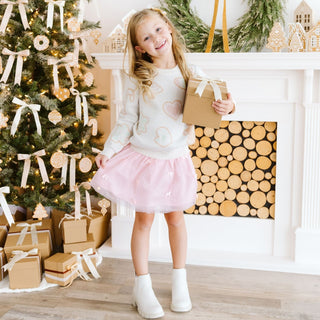 Model wearing Sweet Wink Christmas Cookies sweater with blush bows and tutu skirt, festive holiday design and cozy knit fabric.