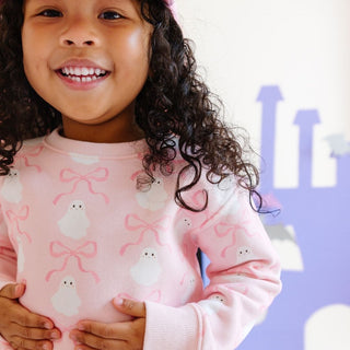 Sweet Wink Coquette Ghost Halloween Sweatshirt & Flare Legging Set Child wearing a pink sweater with bird and bow pattern, standing in front of a castle.