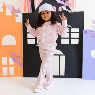 Sweet Wink Coquette Ghost Halloween Sweatshirt & Flare Legging Set
Child in pink Halloween-themed outfit with decorative paper houses in the background