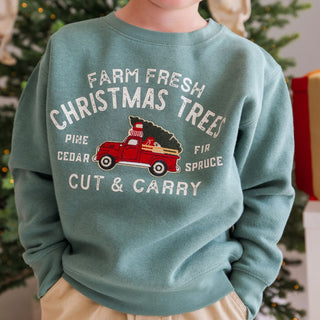 Model wearing Sweet Wink Christmas Tree Patch sweatshirt in khaki, featuring festive tree and truck patches, paired with a beanie.