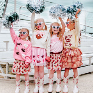 The Coquette Football Sequin Tutu is a fun skirt and dress up tutu for celebrating Game Day!

Features:

Ballet pink tulle and cotton lining
Brown and white sequin footballs and pink sequin bows
Pink glitter elastic waistband
Care: Hand wash and line dry
The Sweet Wink difference:

Super soft tulle that doesn’t scratch or itch
Cotton lining provides extra coverage and comfort
“Shed-free” embellishments ensure glitter does not sprinkle arounFour young girls in matching outfits with pom-poms on a wooden deck.
