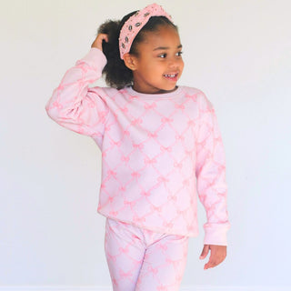 Sweet Wink Bow Trellis Sweatshirt & Flare Legging Set
Young girl wearing a pink and white outfit with bow patterns on a plain background