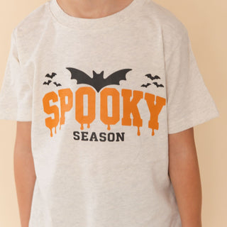 Sweet Wink Spooky Season Halloween Short Sleeve T-Shirt
A child wearing a light heather gray t-shirt with a 'Spooky Season' Halloween graphic featuring dripping orange text, black bats, and black silhouettes on a beige background.