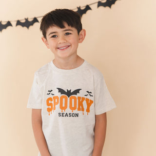 Sweet Wink Spooky Season Halloween Short Sleeve T-Shirt
A young boy smiling and wearing a light gray heather t-shirt with a 'SPOOKY SEASON' graphic in orange and black, posed against a warm beige background with a black bat banner.