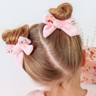 Sweet Wink Sprinkle Bow Clip Set 
Child's hair styled with pink hair bows featuring colorful sprinkles on a white background