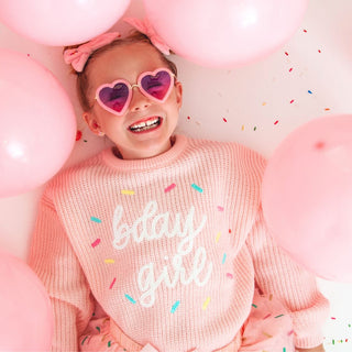Sweet Wink Birthday Girl Sprinkle Knit Sweater 
Child wearing a pink sweater with 'baby girl' text, surrounded by pink balloons and sprinkles.