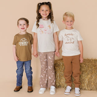 Sweet Wink Western Three children standing together in front of a bale of hay, wearing matching outfits with cowboy-themed text.