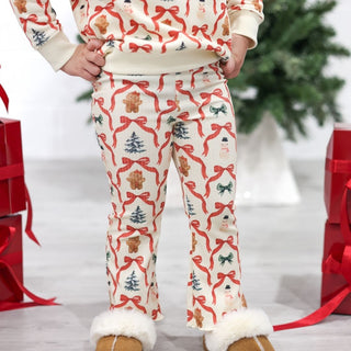 Sweet Wink Christmas Cutie Sweatshirt & Flare Legging Set
Person wearing Christmas-themed pajama set with red bows and white fur cuffs, standing in front of a decorated Christmas tree and presents.