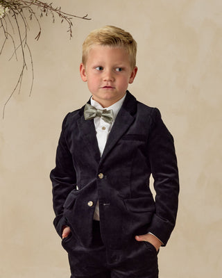 Noralee Sebastian Blazer - Black
Young boy in a formal black suit with a bow tie against a beige background