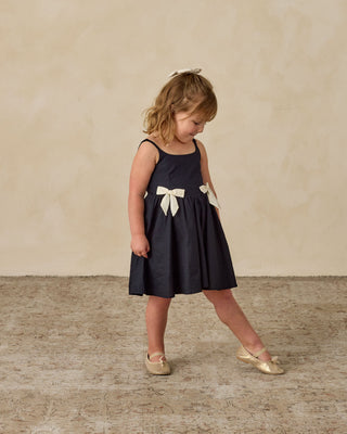 Noralee Betsy Dress - Black
Young girl wearing a black dress with a white bow on a beige background