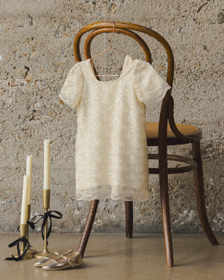 Noralee Daisy Dress - Silver Metallic
White lace dress on a wooden chair with candles and shoes in the foreground.