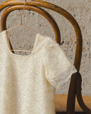 Noralee Daisy Dress - Silver Metallic
Beige lace top on a hanger against a textured wall.