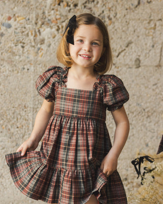 Noralee Louella Dress - Winter Tartan
Young girl wearing a plaid dress with puffed sleeves against a stone wall background