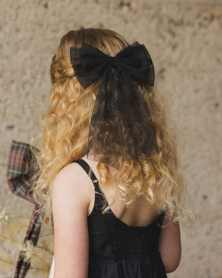 Noralee Alice Bow - Black
Noralee Betsy Dress - Black
Person with long, wavy hair wearing a large black bow, standing against a textured wall.