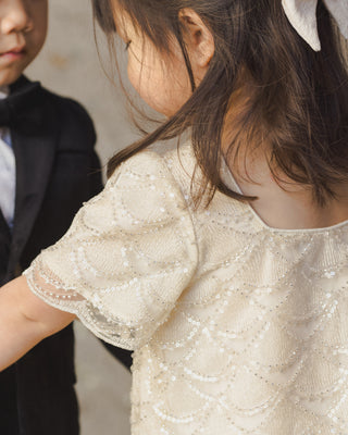 Noralee Daisy Dress - Silver Metallic
Close-up of a child wearing a sparkly white dress with a blurred background