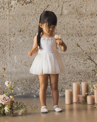 Noralee Clementine Tutu - Ivory
Young girl in a white dress standing in front of a textured wall with flowers and candles.