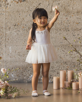 Noralee Clementine Tutu - Ivory
Young girl in a white dress standing against a textured wall with candles and flowers.