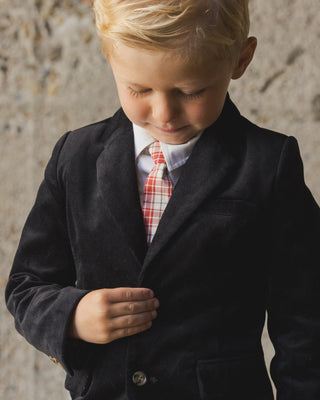 Noralee Sebastian Blazer - Black
Young boy wearing a dark coat over a white shirt with a plaid tie against a stone wall.