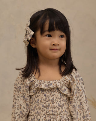 Noralee Norah Bow - Blue Garden
A young girl with dark hair wearing a beige floral-patterned dress and a matching hair bow, photographed against a neutral beige background.