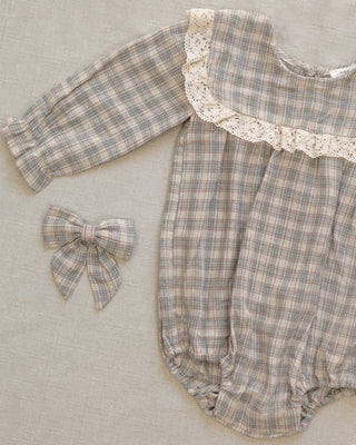 Noralee Noelle Romper - Fall Plaid
A baby romper in a beige and gray plaid fabric with a cream lace collar, shown alongside a matching plaid bow on a textured beige fabric background.