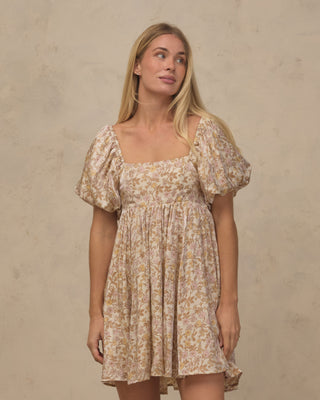 Noralee Women's Vivian Dress - Wildflower
A woman modeling a short puff-sleeve dress with a square neckline and an all-over floral print in beige, cream, and muted yellow, standing against a textured beige wall.