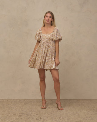 Noralee Women's Vivian Dress - Wildflower
A woman modeling a short puff-sleeve dress with a beige and brown floral pattern, standing against a textured beige studio backdrop.