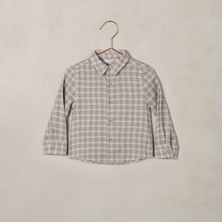 Noralee Harrison Button Down - Fall PlaidA long-sleeve button-up shirt with a small-scale beige and gray plaid pattern, hanging on a wooden hanger against a textured beige wall.