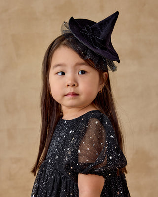 Noralee Luna Dress - Night Sky
Young girl wearing a black witch hat and dress with star patterns on a beige background