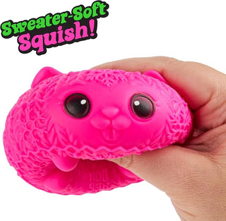 NeeDoh Squishmas KnittensA bright pink, cat-shaped squishy toy being held by a hand against a white background, with a green and black 'Sweater Soft Squish!' text overlay in the top left corner.