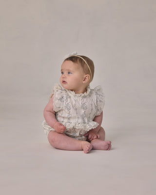 Noralee Alice Romper - French Floral StripeBaby sitting on a plain background wearing a floral romper.