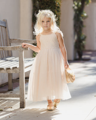 Noralee Camilla Dress - Pearl
Young girl in a light pink dress standing outdoors near a wooden bench.