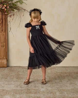 Noralee Clara Dress - Black
Young girl wearing a black dress with a bow, standing against a neutral wall.