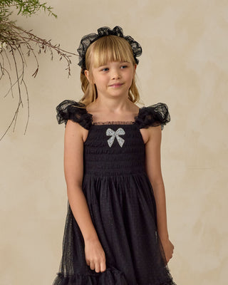 Noralee Clara Dress - Black
Noralee Gathered Headband - Black
Young girl wearing a black dress with a bow and matching headband against a beige background