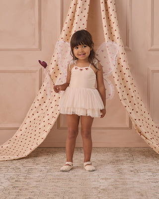 Noralee Clementine Tutu - Pearl
Young girl in a white dress with fairy wings standing in front of a pink curtain.