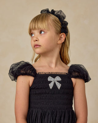 Noralee Gathered Headband - Black Young girl wearing a black dress with a bow and a headband against a beige background