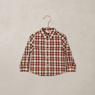 Noralee Harrison Button Down - Holiday Tartan
A long-sleeve button-up shirt with a red and white plaid pattern, hanging on a metal hanger against a textured beige wall.