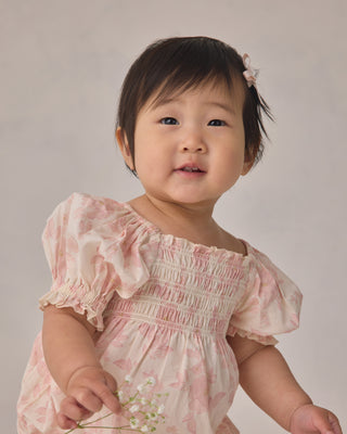 Noralee Hazel Romper - Blush English Rose
Baby in a pink dress with ruffled sleeves against a plain background