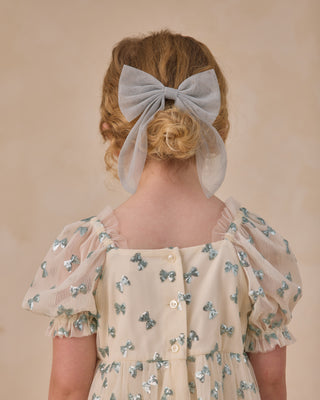 Noralee Louella Dress - Bows
Person wearing a floral dress with butterfly patterns and a large bow in their hair against a beige background