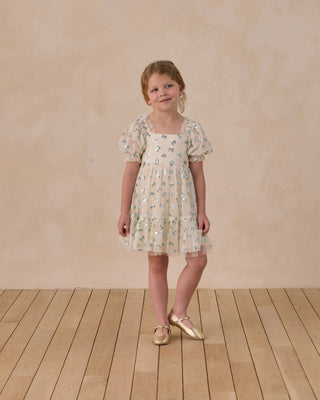 Noralee Louella Dress - Bows
Young girl wearing a floral dress standing on a wooden floor with a beige wall background