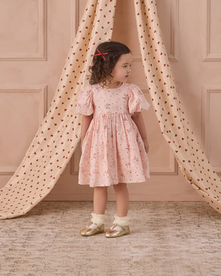 Noralee Luna Dress - Bouquet
Young girl in a pink floral dress standing in front of a pink wall with heart patterns.