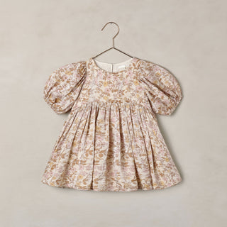 Noralee Luna Dress - Wildflower
A toddler girl's dress with puff sleeves and a gathered smocked bodice, featuring a delicate beige and brown floral toile pattern, hanging on a metal hanger against a textured beige wall.