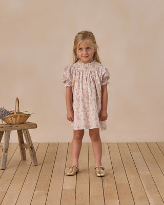 Noralee Maddie Dress - Pastel Garden
Young girl in a floral dress standing in a room with wooden floor and beige wall.