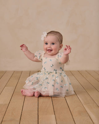 Noralee Margot Romper - Bows
Baby in a floral dress sitting on a wooden floor with a beige background