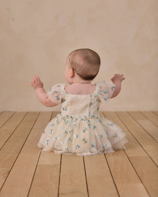Noralee Margot Romper - Bows
Baby in a floral dress standing on a wooden floor with a beige wall background