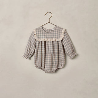 Noralee Noelle Romper - Fall Plaid
A baby long-sleeve romper in a gray and white gingham pattern, featuring a cream lace collar and elasticated cuffs and hem, hanging on a wooden hanger against a textured beige wall.